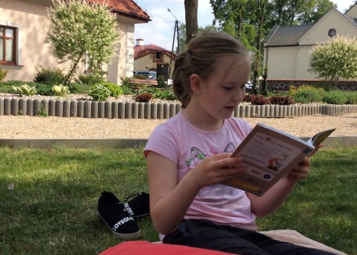 dzieci czytają siedząc na trawniku