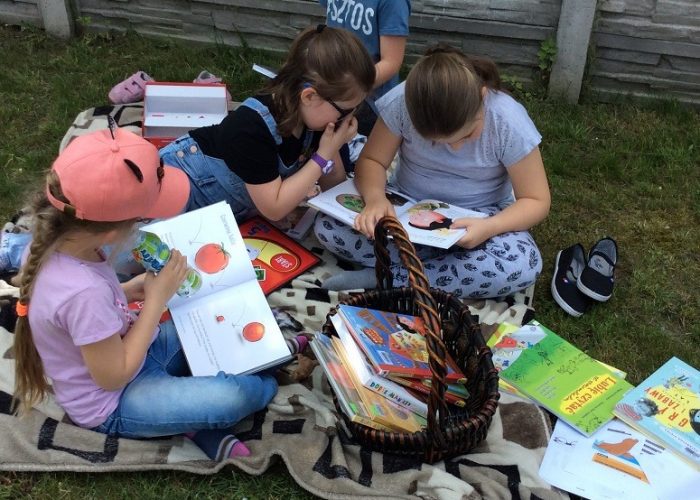 dzieci czytają siedząc na trawniku